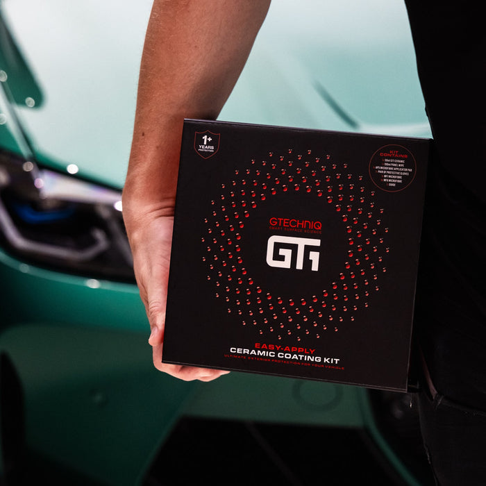A person holding a black GT1 Easy-Apply Ceramic Coating Kit box in front of a teal car.